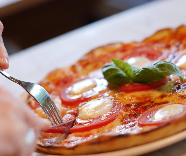 Pizza con pomodori freschi e una foglia di basilico al centro.
