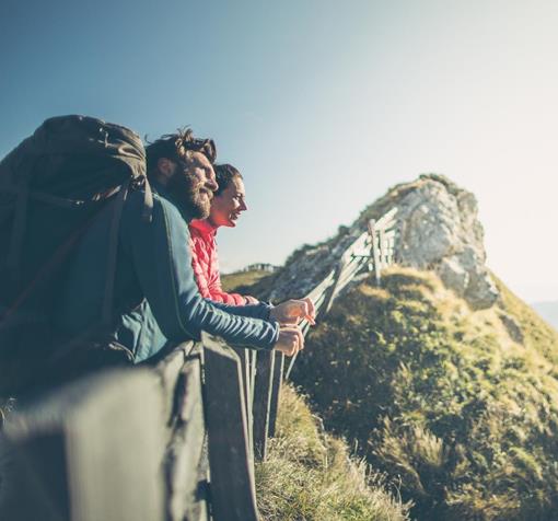 Two hikers with backpacks stand in a sunny alpine mountain landscape and enjoy the panorama.