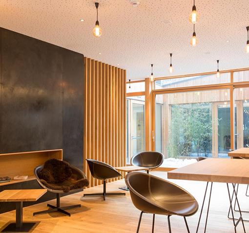 Steindl's Bar Café; Moderner Sitzbereich mit Sesseln, Hochtisch und Barhockern vor einer großen Fensterfront.