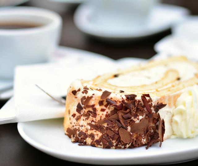 Slice of cake with chocolate shavings and coffee in the background.