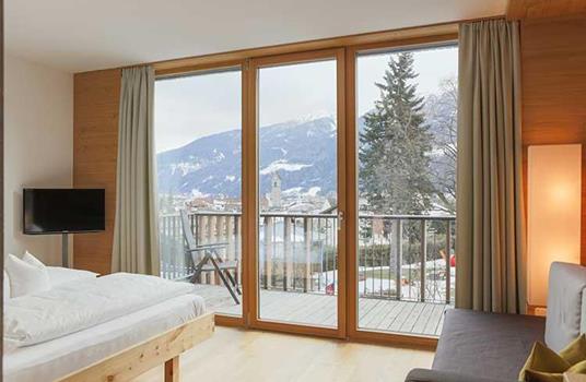 Camera “Wolke” con letto matrimoniale, angolo soggiorno e ampio balcone con vista su Vipiteno e sulle montagne innevate.