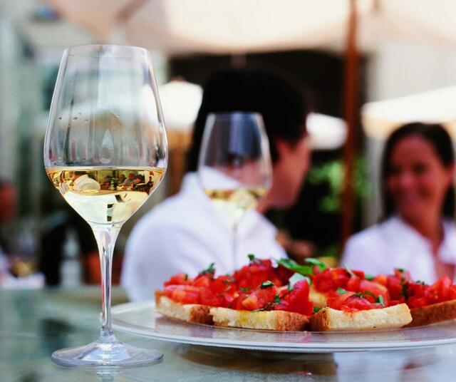 Close-up of two aperitifs and a plate of bruschetta; people are standing in front.