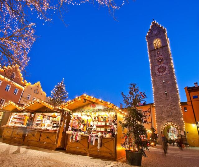 Mercatino di Natale con bancarelle illuminate, albero di Natale e Torre delle Dodici a Vipiteno.