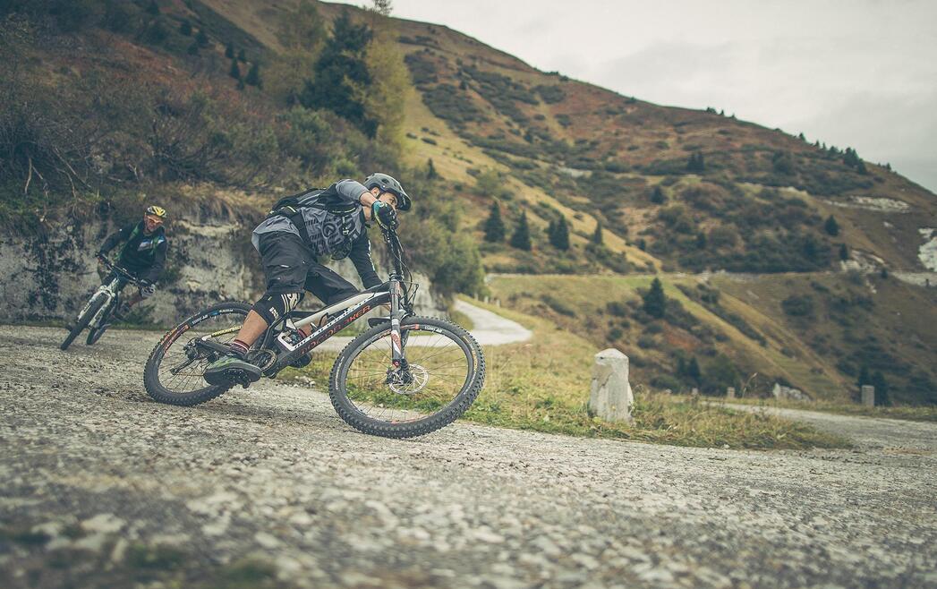 Due mountain biker in discesa su una strada sterrata in un paesaggio alpino