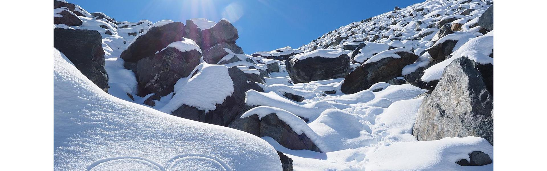 Herz im Schnee vor verschneiter Felslandschaft bei Sonnenschein.
