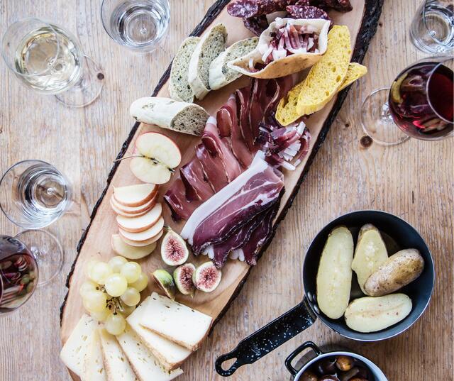 Wooden board with assorted cold cuts and cheeses, bread and side dishes on a set table.