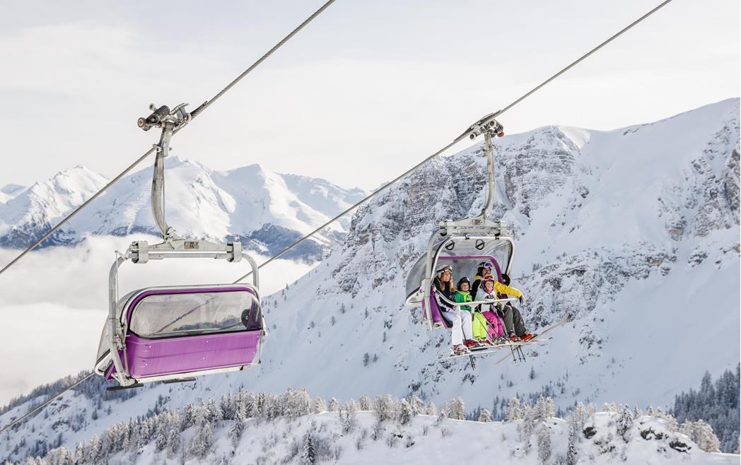 Sessellift mit Skifahrern fährt durch eine verschneite alpine Berglandschaft.