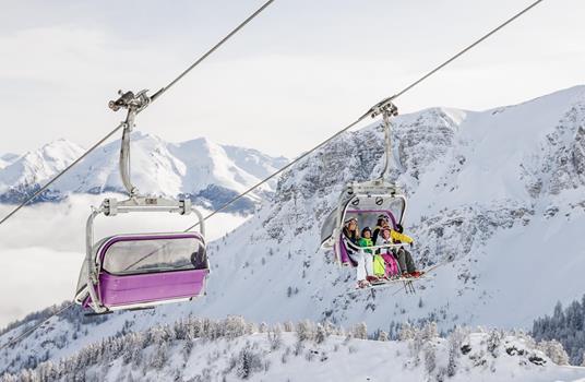 Una seggiovia con sciatori attraversa un paesaggio alpino innevato.