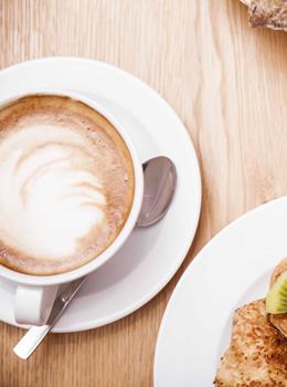 Tavolo apparecchiato per la colazione con cappuccino, prodotti da forno, frutta e succo d’arancia.
