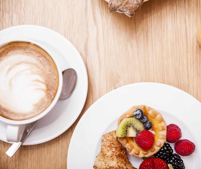 Tavolo apparecchiato per la colazione con cappuccino, prodotti da forno, frutta e succo d’arancia.
