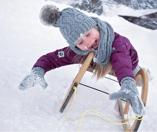 Kind fährt lachend auf einem Holzschlitten durch den Schnee.