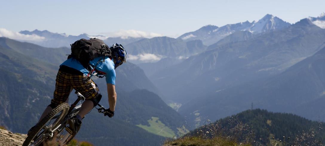 Mountainbiker auf einem steinigen Bergweg; im Hintergrund  sommerliche Berglandschaft