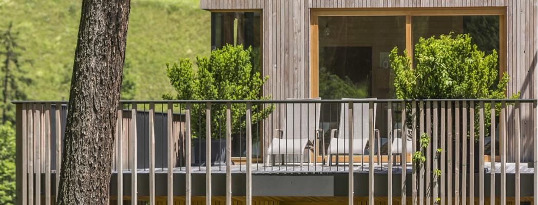 Holzfassade des Steindl's Boutique Hotel mit begrünter Terrasse, Sitzgelegenheiten und Bäumen.