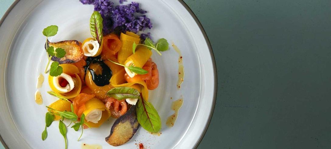 Piatto colorato con verdure, fiori edibili ed erbe aromatiche, servito su un piatto bianco.