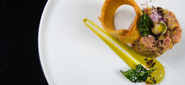 Tartare servita su un piatto bianco con una fetta di pane tostato e un uovo di quaglia.