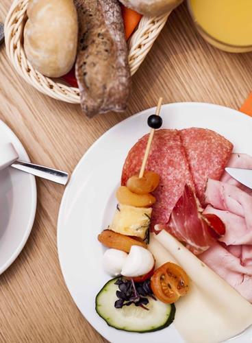 Savoury breakfast with cappuccino, orange juice, a bread basket, cold cuts, cheese and a vegetable skewer.