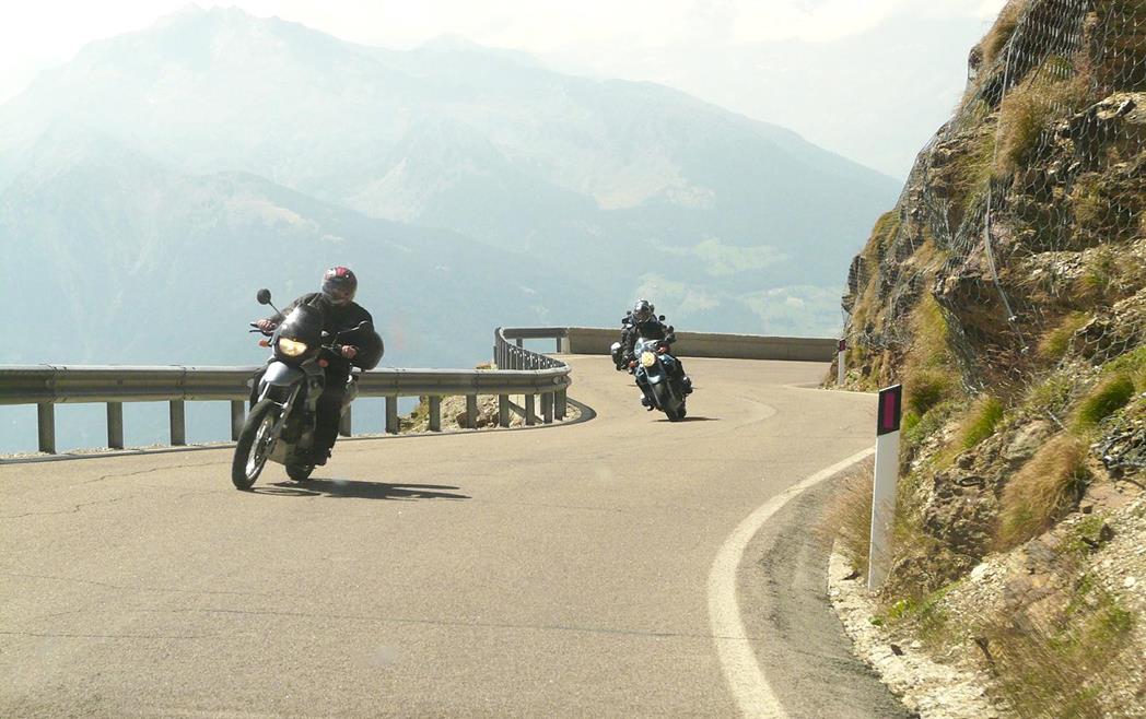 Due motociclisti su una strada tortuosa con montagne sullo sfondo.