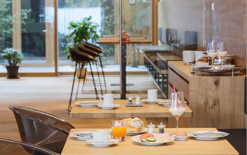Frühstückstische mit Kaffee, Saft, Brotkorb, Teller mit Wurst und Käse mit Blick in den Garten.