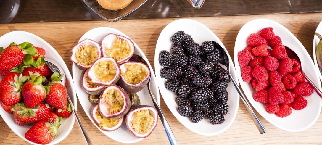 Diversi tipi di frutta in piccole ciotole, con pancake sullo sfondo.