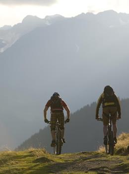 Zwei Mountainbiker auf einem Bergweg vor alpinem Panorama.
